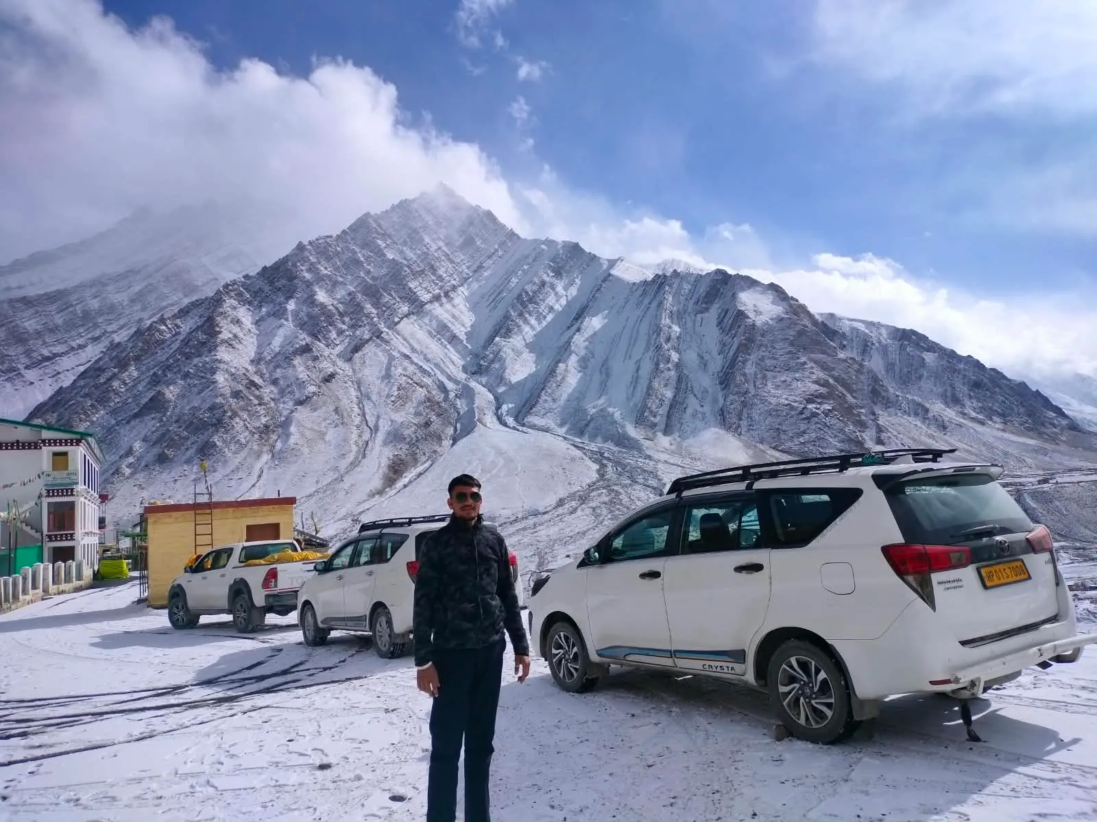 Kulwant standing beside white SUVs in a snow-covered parking area, a striated snowy peak rising behind